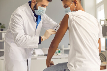 Young doctor in face mask giving coronavirus or flu antiviral vaccine to patient