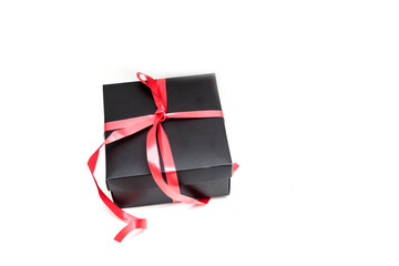 Black gift box with red satin ribbon and bow, over white background.