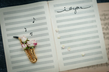 Golden saxophone with rose on background of music note-book. Jazz day concept. Space for text, top...
