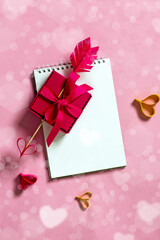 Valentine's day background from notepad, arrow heart and gift box. Valentine's day romantic background concept from gift box with homemade arrow with paper heart. Top view, copy space