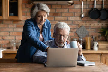 Smiling older mature hoary woman pointing finer at laptop screen, choosing holidays trip with...