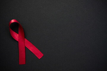 Red ribbon as symbol of aids awareness on black background. Medical care campaign 