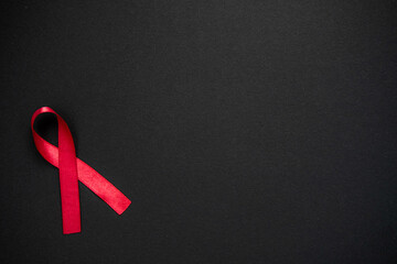 Red ribbon as symbol of aids awareness on black background. Medical care campaign 