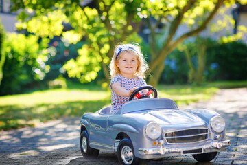 Little adorable toddler girl driving big vintage toy car and having fun with playing outdoors....