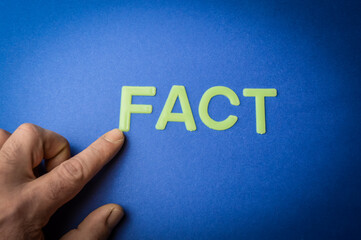Human finger pointing the word Fact written with plastic letters on blue paper background, concept
