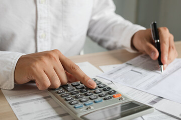 Close up hand of young asian man is pressing a calculator to calculate cost from invoice/bills or statement to plan his spending for payday.
