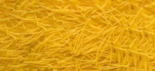 Obraz premium Raw vermicelli pasta background. raw yellow vermicelli is scattered on the table. short raw yellow vermicelli for cooking. banner