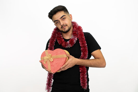 Young man is holding a heart-shaped gift box in his hands. Isolated image and white background.