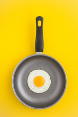 Top view of frying pan with fried egg on the yellow background