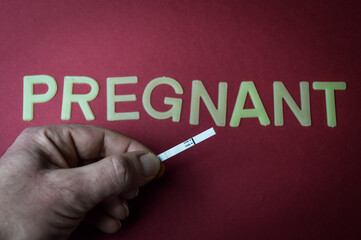 Human fingers holding a pregnancy test over the word Pregnant, written with plastic letters on a...