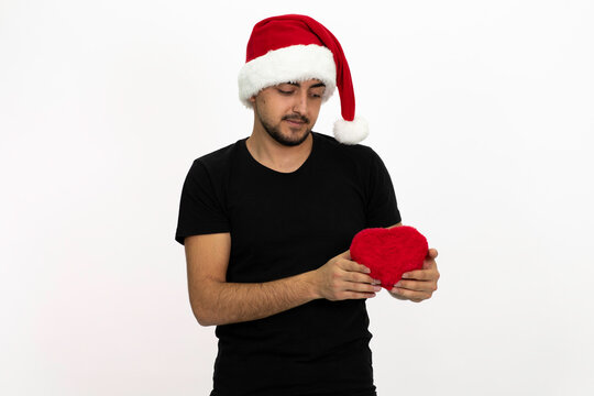Young male with a santa hat. Young man is holding a heart-shaped gift box in his hands. Isolated image and white background.