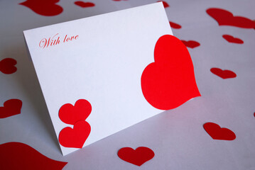 A white envelope with a red heart for Valentine's Day surrounded by small hearts on a white background.