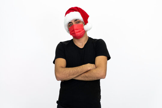 Young man wearing a Santa hat. There is a red medical mask. He is wearing a black shirt. Isolated image white background.