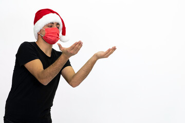 Fototapeta na wymiar Young man wearing a Santa hat. There is a red medical mask. He is wearing a black shirt. Isolated image white background.