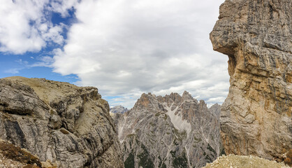 A Sphinx-like rock formation in Italian Dolomites. The mountain resembles a human face. Raw and unspoiled landscape. Few clouds above the peaks. High mountain peaks in the back. Serenity