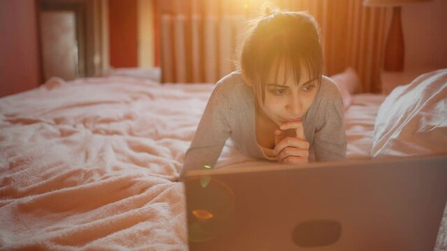 camera zooming to pretty woman freelancer or student lying on bed using portable laptop computer for distance work or study during quarantine. stay home, remote work, watching, online education.