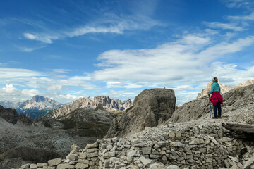 A woman hiking in high and desolated mountains in Italian Dolomites. She stands at the edge of a slope and enjoys the idyllic landscape. Raw and unspoiled landscape. Sunny day. Endless mountain chains