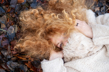 Portrait of beautiful red haired woman, redhead, lying with sweater and fur scarf in the dark autumn leaves, copy space