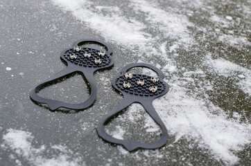 Ice Grippers Cleats for Shoes and Boots on slippery road with frozen puddle covered with ice. Anti...