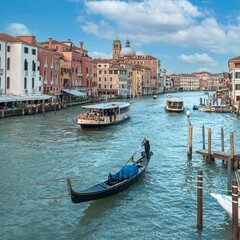 gondola and tourist ships sailing along the Grand Canal in Venice against the backdrop of beautiful houses and blue sky