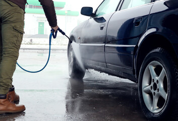 A man's hand directs a stream of water to the wheel of the car, side view-the concept of using car service services in car care