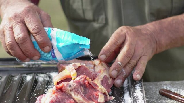 Salting raw meat, in slow motion, on the outskirts of the field.