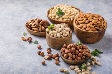 Assortment of nuts in a wooden bowls, on a gray background. Hazelnuts, pistachios, almonds, brazil nut, cashews