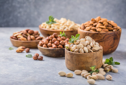 Assortment of nuts in a wooden bowls, on a gray background. Hazelnuts, pistachios, almonds, brazil nut, cashews