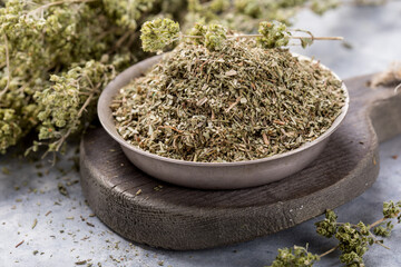 Bowl of dried oregano leaves on stone background.