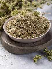 Bowl of dried oregano leaves on stone background.