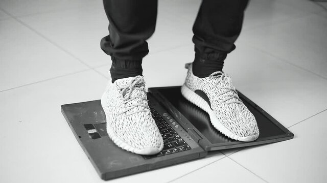 The programmer jumps with his feet in anger on an old laptop that worked slowly, black and white video