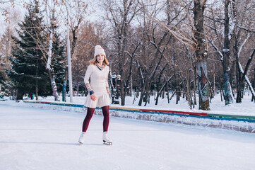 Young blonde caucasian girl in warm clothes skating on frozen lake in snowy winter park