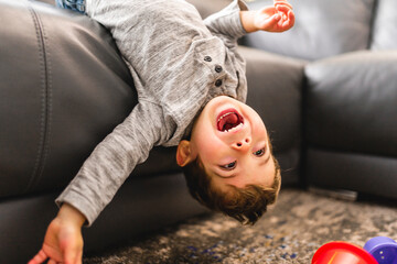 Little boy is standing on sofa at home upside down