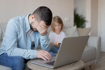 Man working from home on laptop with kid daughter who sitting on sofa with smartphone. Man stressed with computer works at home. Remote work. Online education. Quarantine and self isolation.