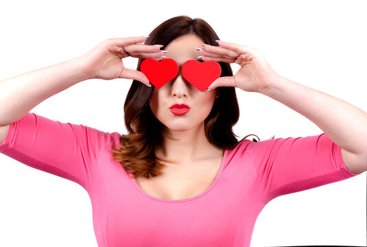 A pretty woman is holding two red valentine hearts in front of her eyes. Isolated. white background.