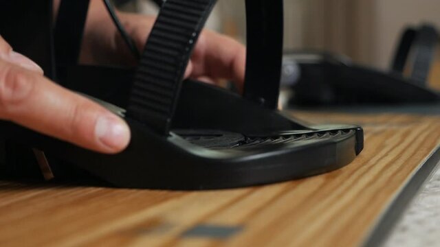The man's hand attaches the bindings to the snowboard. Prepares the snowboard for winter