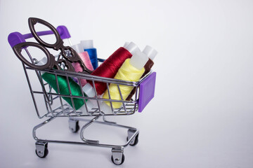 Mini decorative shopping cart with with colored threads for sewing and scissors on white background. With copy space