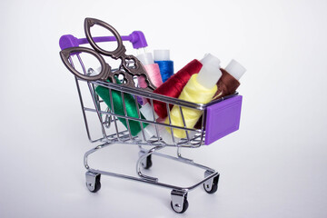 Mini decorative shopping cart with with colored threads for sewing and scissors on white background.