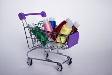 Mini decorative shopping cart with with colored threads for sewing on white background.