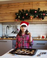 The girl in the kitchen is standing next to a tray of cookies