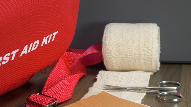 Close POV reverse dolly shot of a first aid kit box, with various items on a table &ndash; bandage, scissors, sticking plasters and a bottle of ointment.