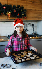 a girl in the kitchen holds a tray of cookies in her hands