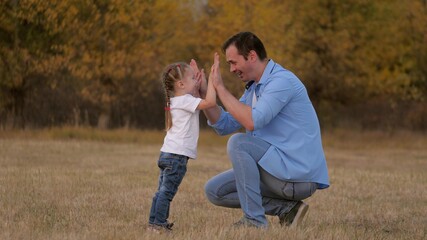 Dad plays with his little daughter teaches to shake hands, hello daddy. Father and beloved child are having fun together. Happy family concept. kid and parent are having fun in park. Walk outdoors