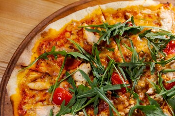 pizza with arugula, meat and tomatoes on a wood plate for restaurant menu