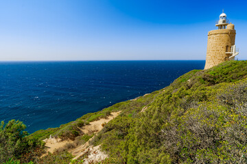 Fototapeta na wymiar Faro sobre una colina en un acantilado sobre el mar un día soleado con cielo azul. Desde Zahara de los Atunes, Cádiz, Andalucía, España.