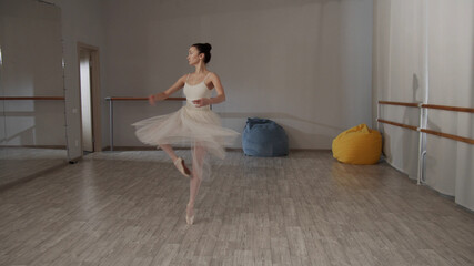 Charming ballerina in the dance hall in front of the mirror in a beautiful dress doing pirouettes