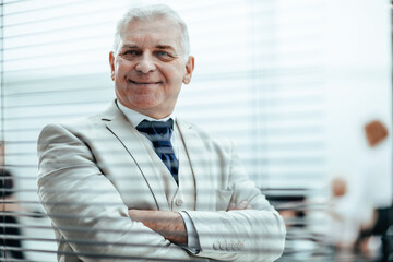 smiling Mature businessman looking through office window blinds.