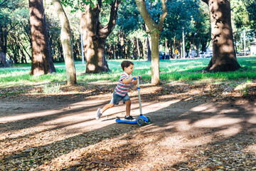 Outdoor activity for children. Little boy on kick scooter in park. Preschool kid learn to skate...