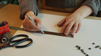 A tailor marks out a sheet of paper with a pencil for making patterns of author's shoes for a family business.