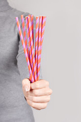 Hand with red coctail straw on grey background.